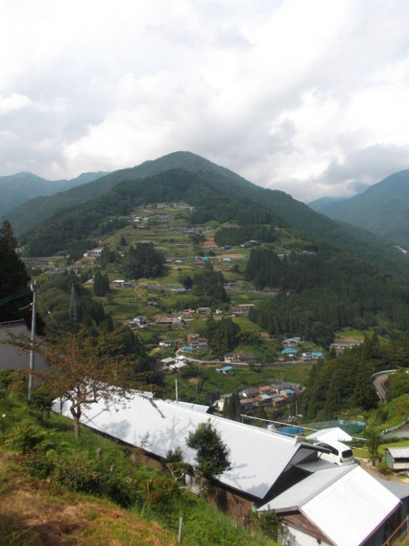 There is a tall green mountain, with a long switch-backed road creeping up its face.  Along the road is a village with many traditional Japanese farmhouses